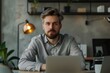 © inspiretta - A man with a beard is sitting at a desk with a laptop in front of him. He is wearing a gray shirt and he is focused on his work