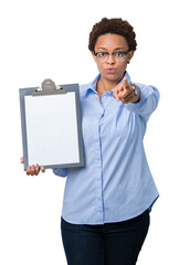 Sticker - Young african american businesss woman holding clipboard over isolated background pointing with finger to the camera and to you, hand sign, positive and confident gesture from the front