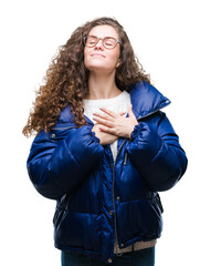 Sticker - Beautiful young brunette curly hair girl wearing winter coat, glasses and sweater over isolated background smiling with hands on chest with closed eyes and grateful gesture on face. Health concept.