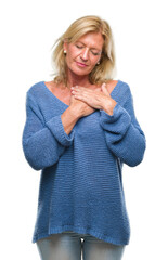 Poster - Middle age blonde woman wearing winter sweater over isolated background smiling with hands on chest with closed eyes and grateful gesture on face. Health concept.