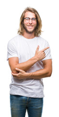 Canvas Print - Young handsome man with long hair wearing glasses over isolated background cheerful with a smile of face pointing with hand and finger up to the side with happy and natural expression on face