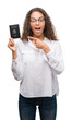 © Krakenimages.com - Young hispanic woman holding passport of United States of America very happy pointing with hand and finger