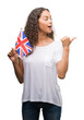 © Krakenimages.com - Young hispanic woman holding flag of United Kingdom pointing and showing with thumb up to the side with happy face smiling