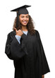 © Krakenimages.com - Young hispanic woman wearing graduation uniform happy with big smile doing ok sign, thumb up with fingers, excellent sign