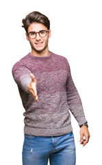 Wall Mural - Young handsome man wearing glasses over isolated background smiling friendly offering handshake as greeting and welcoming. Successful business.