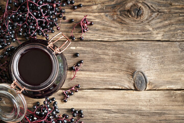 Poster - Homemade black elder syrup in a glass jar with fresh elderberries on wooden background with copy space