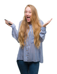 Canvas Print - Blonde teenager woman using smartphone very happy and excited, winner expression celebrating victory screaming with big smile and raised hands