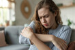 © Klay - young woman suffering from sharp pain in arm sitting in a cozy living room