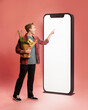 © master1305 - Young man with groceries in hands, interacting with large smartphone with empty white screen against pink background. Concept of online shopping, food, delivery service, app