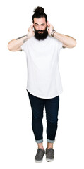 Sticker - Young hipster man with long hair and beard wearing casual white t-shirt covering ears with fingers with annoyed expression for the noise of loud music. Deaf concept.