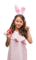 Poster - Brunette hispanic girl wearing easter rabbit ears surprised with an idea or question pointing finger with happy face, number one