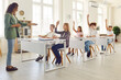 © Studio Romantic - High school students sitting at the desks in the classroom with a friendly happy woman teacher and raising hands up to ask or answer a question during a lesson. Back to school, education concept