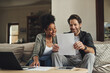 © aLListar/peopleimages.com - Couple, paperwork and planning on sofa with laptop for online tax registration, insurance application and savings in home. Interracial lovers, computer and documents for finance, bills and loan form