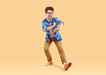 Full size photo of cheerful guy enjoying dance. Funny happy bearded young man in eyeglasses wearing casual clothes having fun over isolated beige studio background