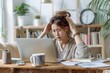 © MD Media - Upset and angry woman sitting at her desk, holding her head as if she is feeling unwell or stressed due to work
