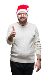 Wall Mural - Young caucasian man wearing christmas hat and glasses over isolated background doing happy thumbs up gesture with hand. Approving expression looking at the camera with showing success.