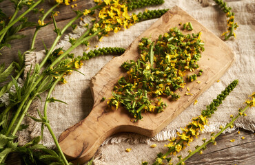 Wall Mural - Chopped fresh agrimony flowers on a wooden cutting board - ingredient for herbal tincture