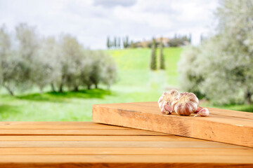 Poster - Empty wooden cutting board on and wooden table background with copy space for food and products. Image for montage objects display. Green ladscape of big green garden fields in distance.