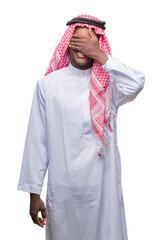 Poster - Young arabic african man wearing traditional keffiyeh over isolated background smiling and laughing with hand on face covering eyes for surprise. Blind concept.