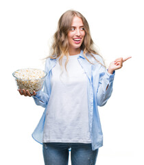 Wall Mural - Beautiful young blonde woman eating popcorn over isolated background very happy pointing with hand and finger to the side