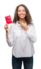 Sticker - Young hispanic woman holding passport of Switzerland very happy pointing with hand and finger