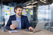 © Liubomir - Confident businessman working with digital tablet and laptop in modern office. Professional wearing formal attire, focusing on work tasks, surrounded by sticky notes on glass walls