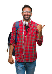 Adult hispanic student man wearing headphones and backpack over isolated background smiling with happy face looking and pointing to the side with thumb up.