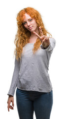 Wall Mural - Young redhead woman smiling looking to the camera showing fingers doing victory sign. Number two.