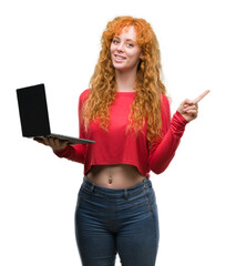 Wall Mural - Young redhead woman using computer laptop very happy pointing with hand and finger to the side