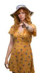 Poster - Young redhead woman wearing summer hat and dress pointing with finger to the camera and to you, hand sign, positive and confident gesture from the front