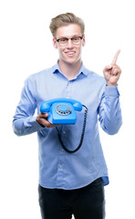 Wall Mural - Young handsome blond man holding vintage telephone very happy pointing with hand and finger to the side