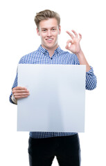 Wall Mural - Young handsome blond man holding a banner doing ok sign with fingers, excellent symbol