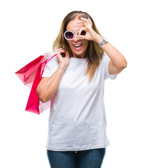 Canvas Print - Middle age hispanic woman holding shopping bags on sales over isolated background with happy face smiling doing ok sign with hand on eye looking through fingers