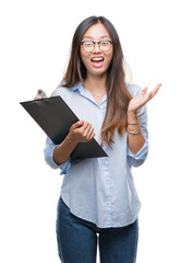 Canvas Print - Young asian business woman holding clipboard over isolated background very happy and excited, winner expression celebrating victory screaming with big smile and raised hands