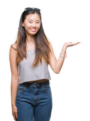 Sticker - Young asian woman wearing sunglasses over isolated background smiling cheerful presenting and pointing with palm of hand looking at the camera.