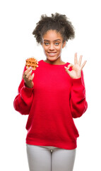 Sticker - Young beautiful afro american woman eating waffle over isolated background doing ok sign with fingers, excellent symbol