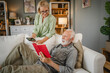 © Miljan Živković - Senior husband lying down on sofa and read book whit his mature wife