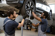 © sofiko14 - Two mechanics in auto repair shop working together on car wheel maintenance. Image depicts teamwork, automotive expertise, and professional service.