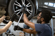 © sofiko14 - Mechanics using tools to fix car wheel in auto repair shop. Teamwork in automotive maintenance and tire repair. Close-up of workers' hands and tools.