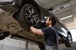© sofiko14 - Mechanic in auto repair shop adjusting car tire on lift using professional tools. Image depicts vehicle maintenance, tire service, and automotive expertise.