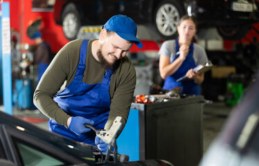 Wall Mural - Young guy mechanic in uniform repairs car in car service station