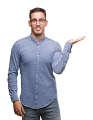 Poster - Handsome young elegant man wearing glasses smiling cheerful presenting and pointing with palm of hand looking at the camera.