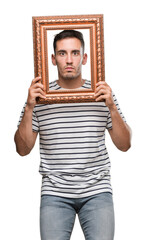 Wall Mural - Handsome young man looking through vintage art frame with a confident expression on smart face thinking serious