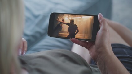 Poster - caucasian woman watches action movie using smartphone while lying on sofa. mobile phone screen with 