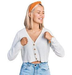 Canvas Print - Beautiful young blonde woman wearing casual white sweater very happy and excited doing winner gesture with arms raised, smiling and screaming for success. celebration concept.