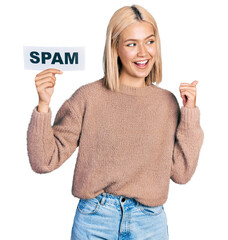 Sticker - Beautiful young blonde woman holding spam banner pointing thumb up to the side smiling happy with open mouth