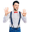 © Krakenimages.com - Hispanic man with beard wearing hipster look with bow tie and suspenders showing and pointing up with fingers number nine while smiling confident and happy.