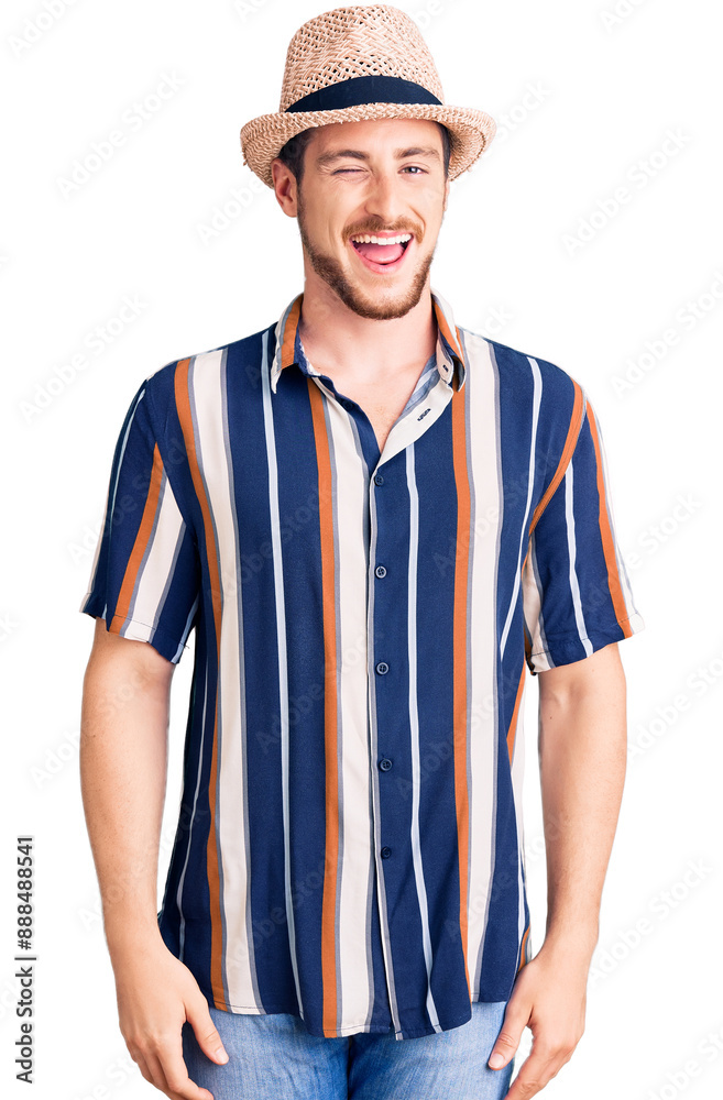Young handsome caucasian man wearing summer hat winking looking at the camera with sexy expression, cheerful and happy face.