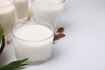 Different types of vegan milk and ingredients on white table, closeup