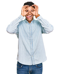 Sticker - Young handsome african american man wearing casual clothes doing ok gesture like binoculars sticking tongue out, eyes looking through fingers. crazy expression.